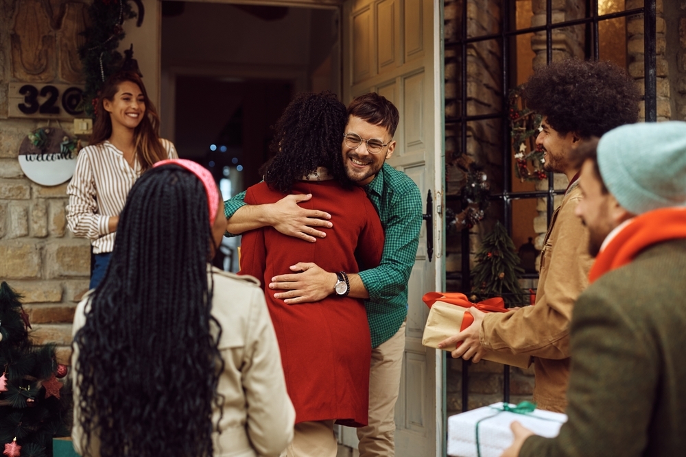 Happy,Couple,Welcoming,Guests,At,The,Doorstep,Of,Their,House.
